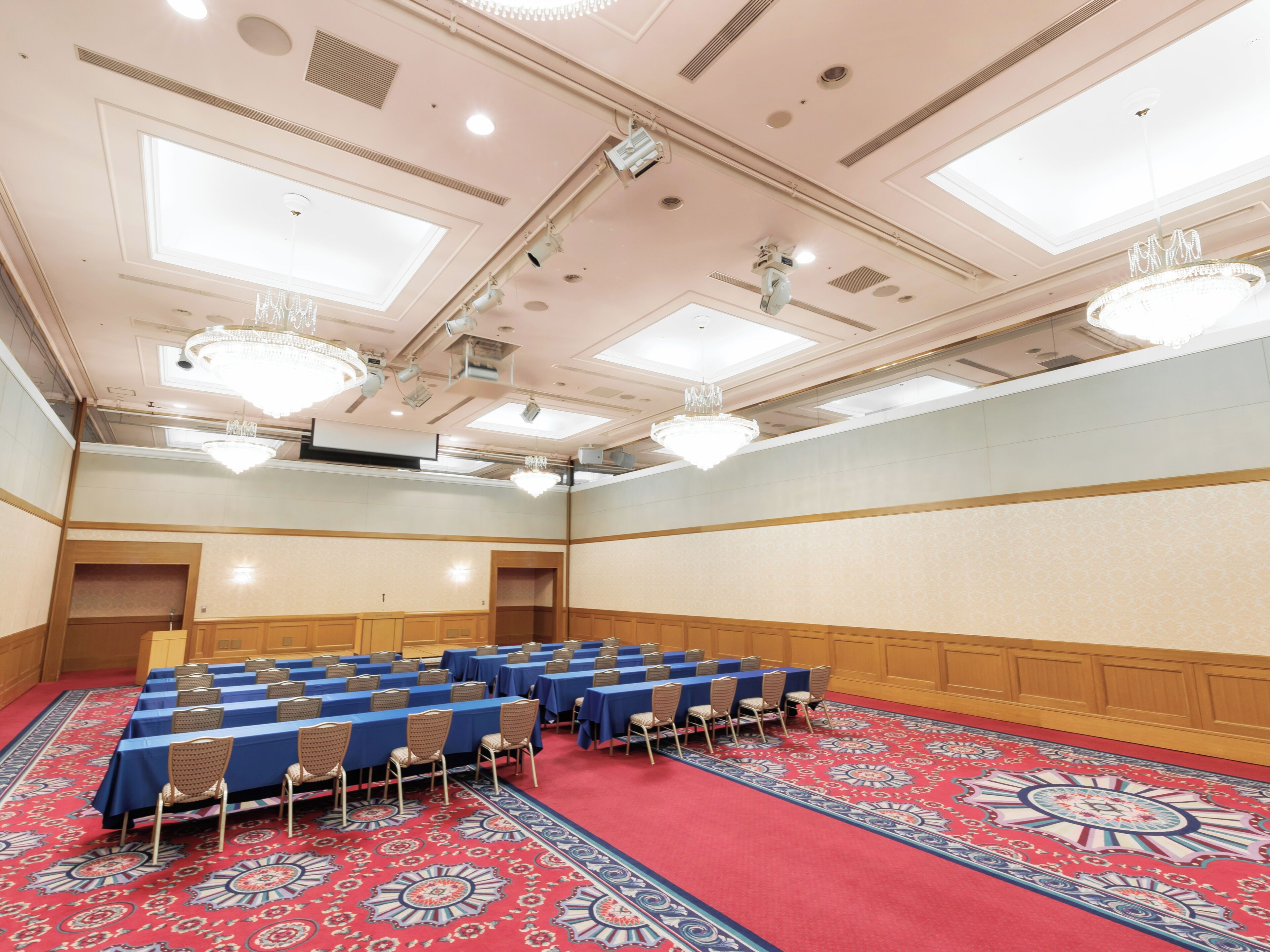 Ein Konferenzraum mit Tischen und Stühlen, einem gemusterten Teppich und Kronleuchtern.
