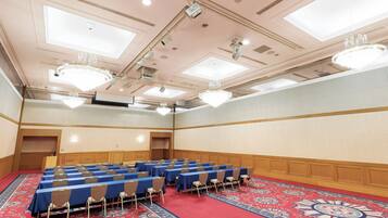 Ein Konferenzraum mit Tischen und Stühlen, einem gemusterten Teppich und Kronleuchtern.