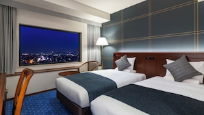 Une chambre d’hôtel avec deux lits, une grande fenêtre donnant sur la ville, un bureau et une chaise.