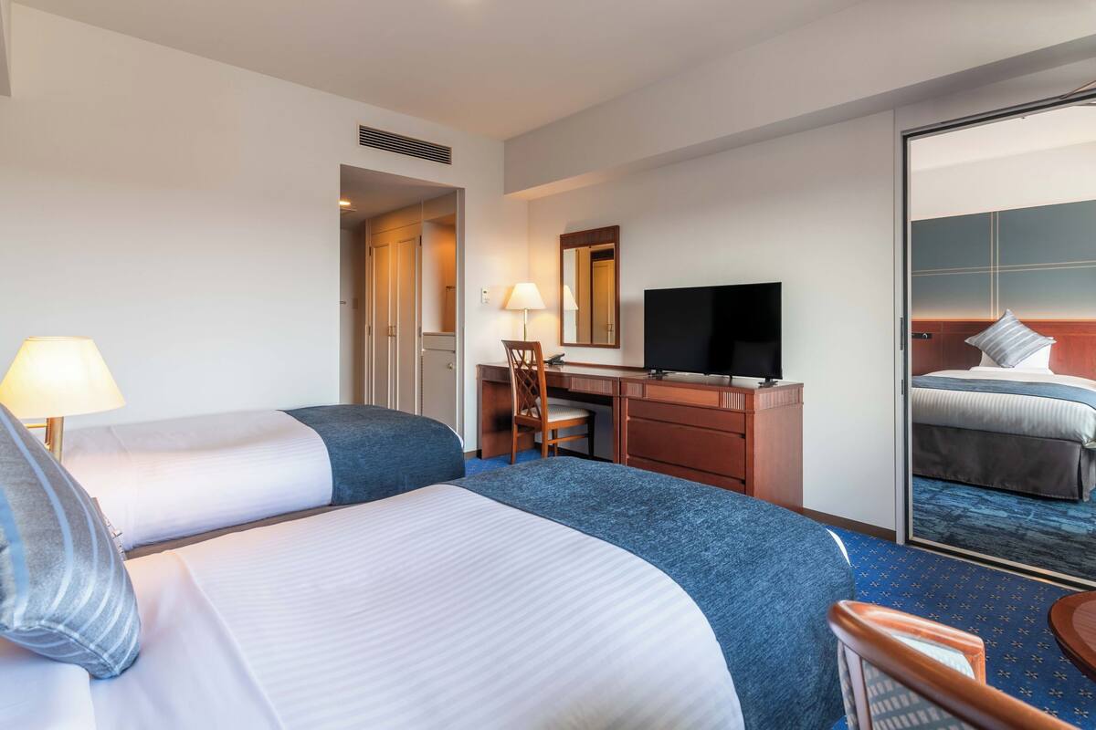 A hotel room with two beds, a desk with a chair, a television, and a large mirror.