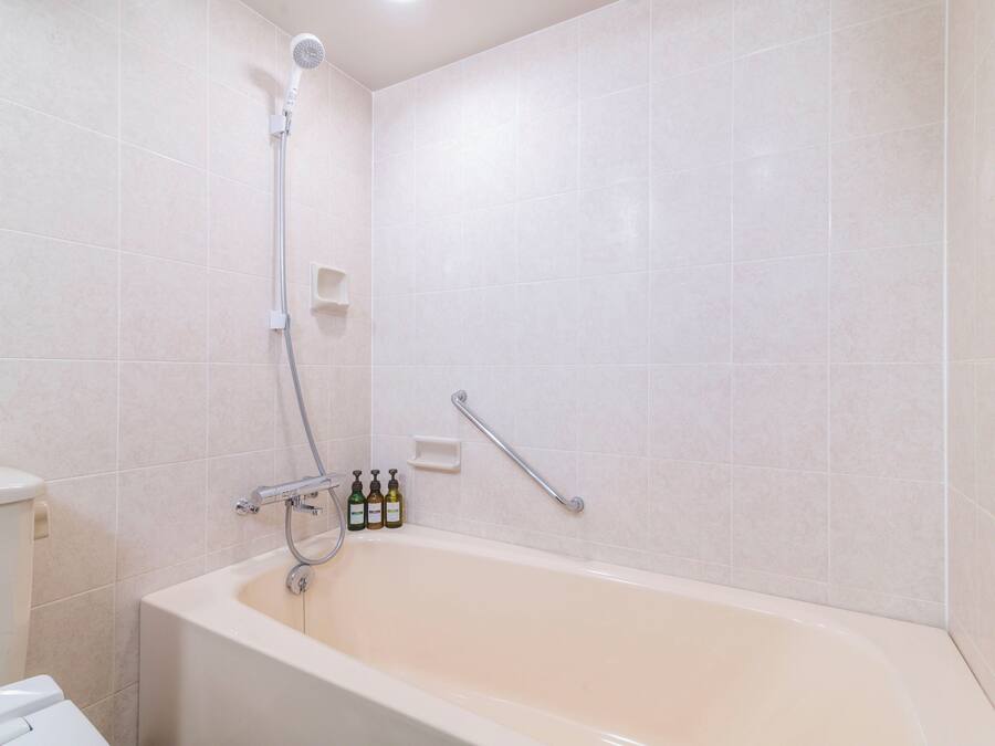 A modern bathroom with a bathtub, a showerhead, and a handrail.