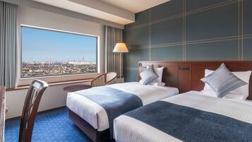 A hotel room with two beds, a view of a cityscape, a desk, and a chair.