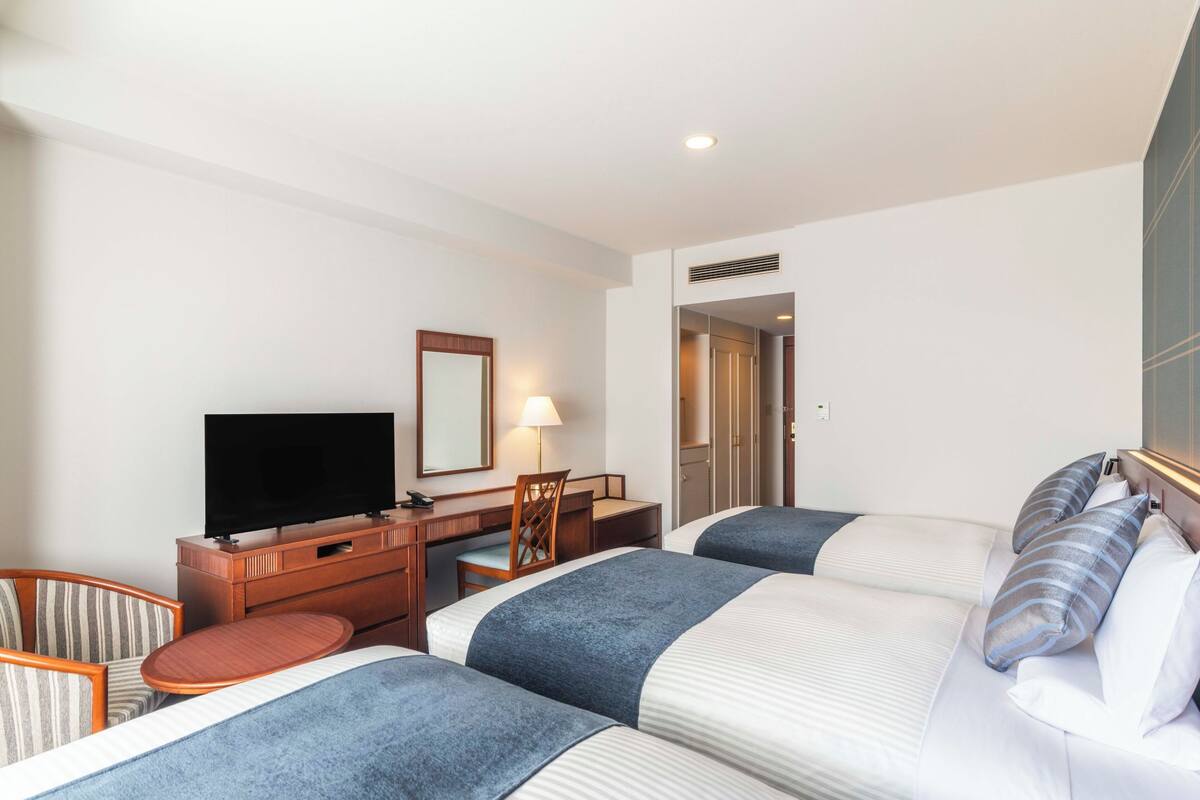 A hotel room with two beds, a TV, a desk, and a chair.