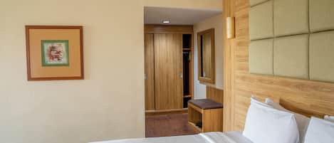 A hotel room with a bed, a wooden wardrobe, a mirror, and a framed picture on the wall.