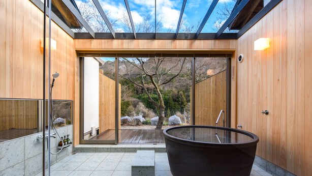 A modern bathroom with a glass-enclosed shower, a large bathtub, and a view of a natural landscape. - Kinshuusanso (Kawaba)