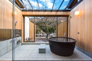 A modern bathroom with a glass-enclosed shower, a large bathtub, and a view of a natural landscape.