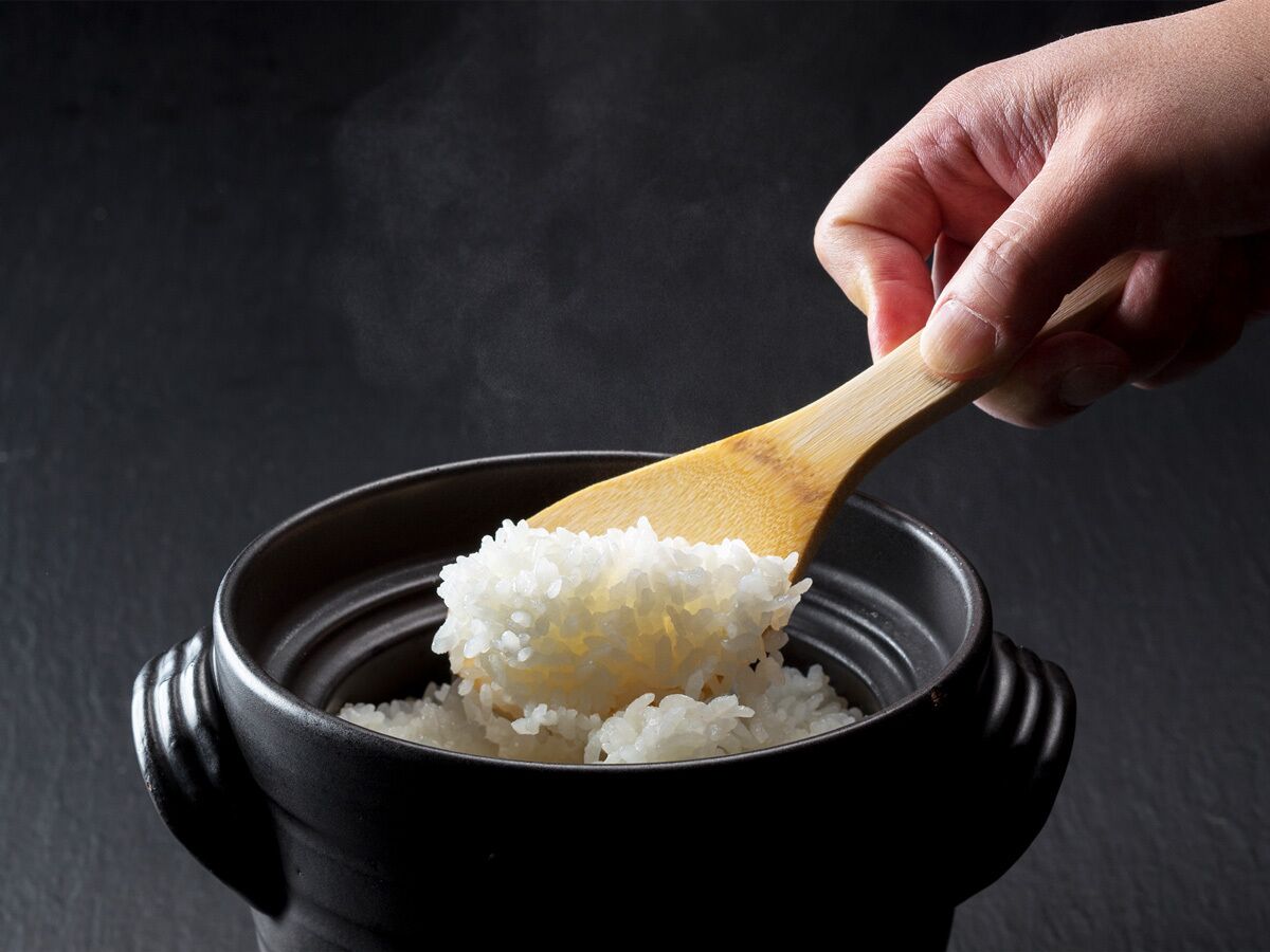 A hand scooping white rice from a black pot.