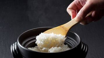 A hand scooping white rice from a black pot.