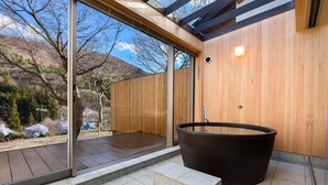 A modern bathroom with a large bathtub, wooden walls, and a glass door leading to an outdoor area with a view of trees and hills. - Kinshuusanso (Kawaba)