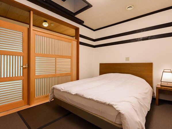 A hotel room with a bed, wooden wardrobe, and a nightstand with a lamp.