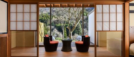 A traditional Japanese room with tatami flooring, a shoji screen door, and a view of a forested area.
