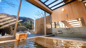 A modern spa with a wooden interior, a large glass window, and a hot tub. - Kinshuusanso (Kawaba)