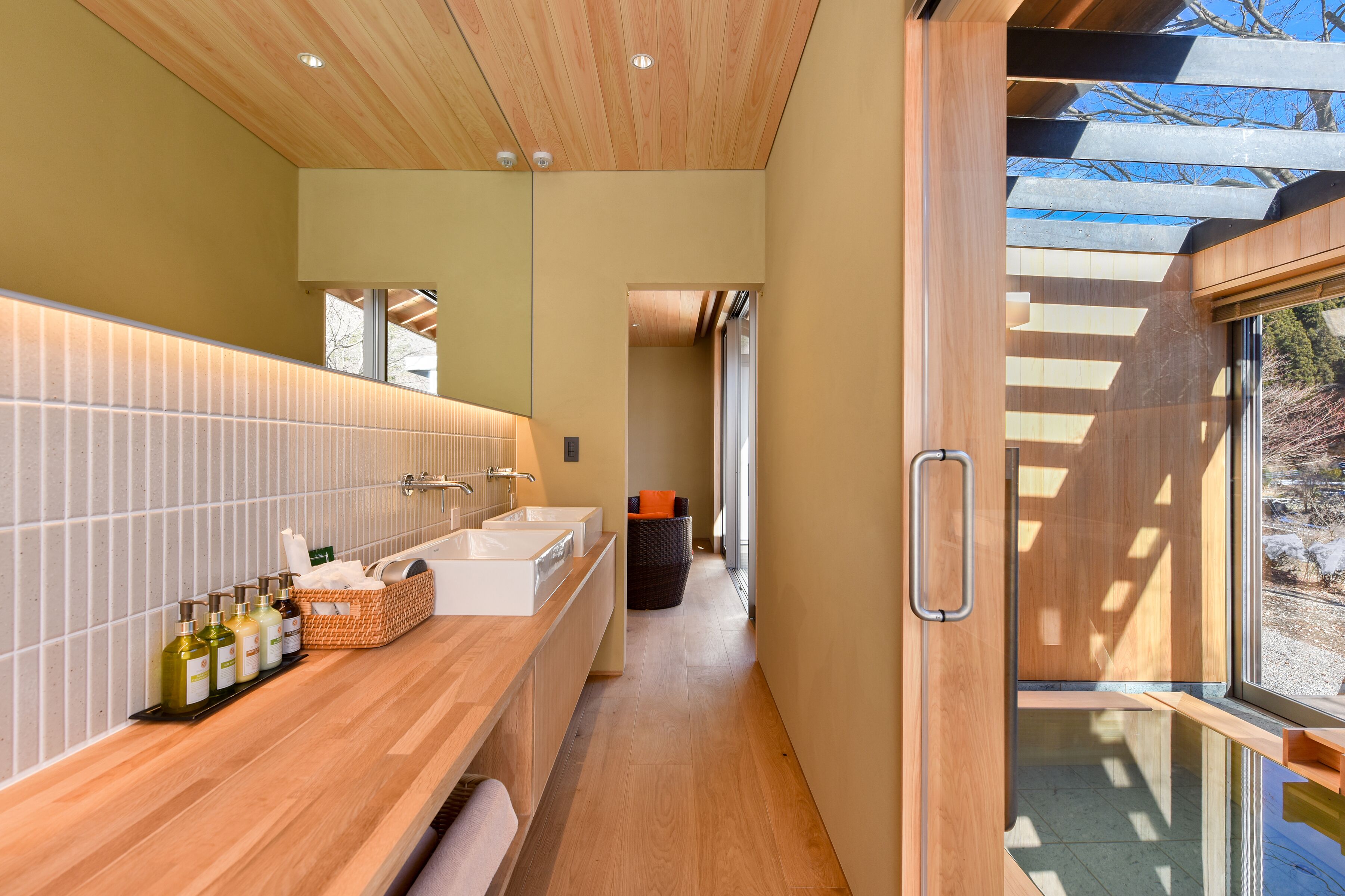 A modern bathroom with a wooden vanity, a large mirror, and a window providing a view of the outdoors.