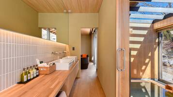 A modern bathroom with a wooden vanity, a large mirror, and a window providing a view of the outdoors.
