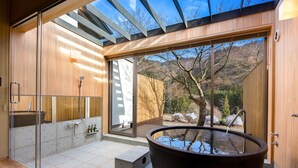 A modern bathroom with a glass shower enclosure, a large bathtub, and a view of the outdoors. - Kinshuusanso (Kawaba)