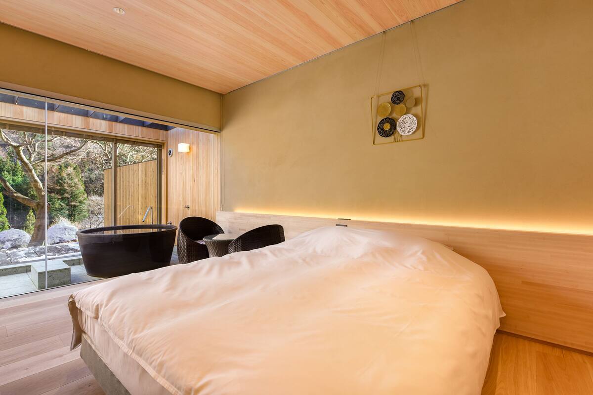 A modern bedroom with a large bed, a bathtub, and a seating area by a large window.