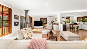 A spacious living room with a large sofa, a television, and a kitchen area with a dining table and bar stools. - Relax with your Best Friend in the heart of Tilba (Central Tilba)