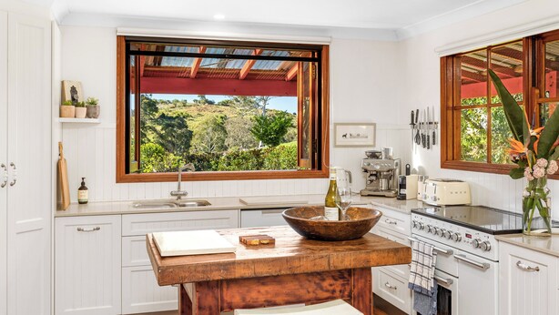 A modern kitchen with white cabinetry, a wooden island, a large window with a view of greenery, and a built-in oven. - Relax with your Best Friend in the heart of Tilba (Central Tilba)