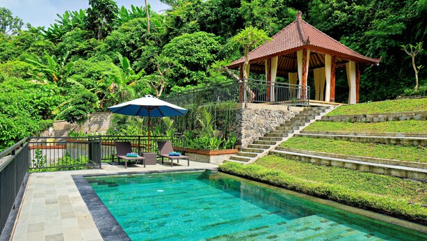 Ein Pool mit klarem Wasser, umgeben von einer Steindeck und einem Pavillon.