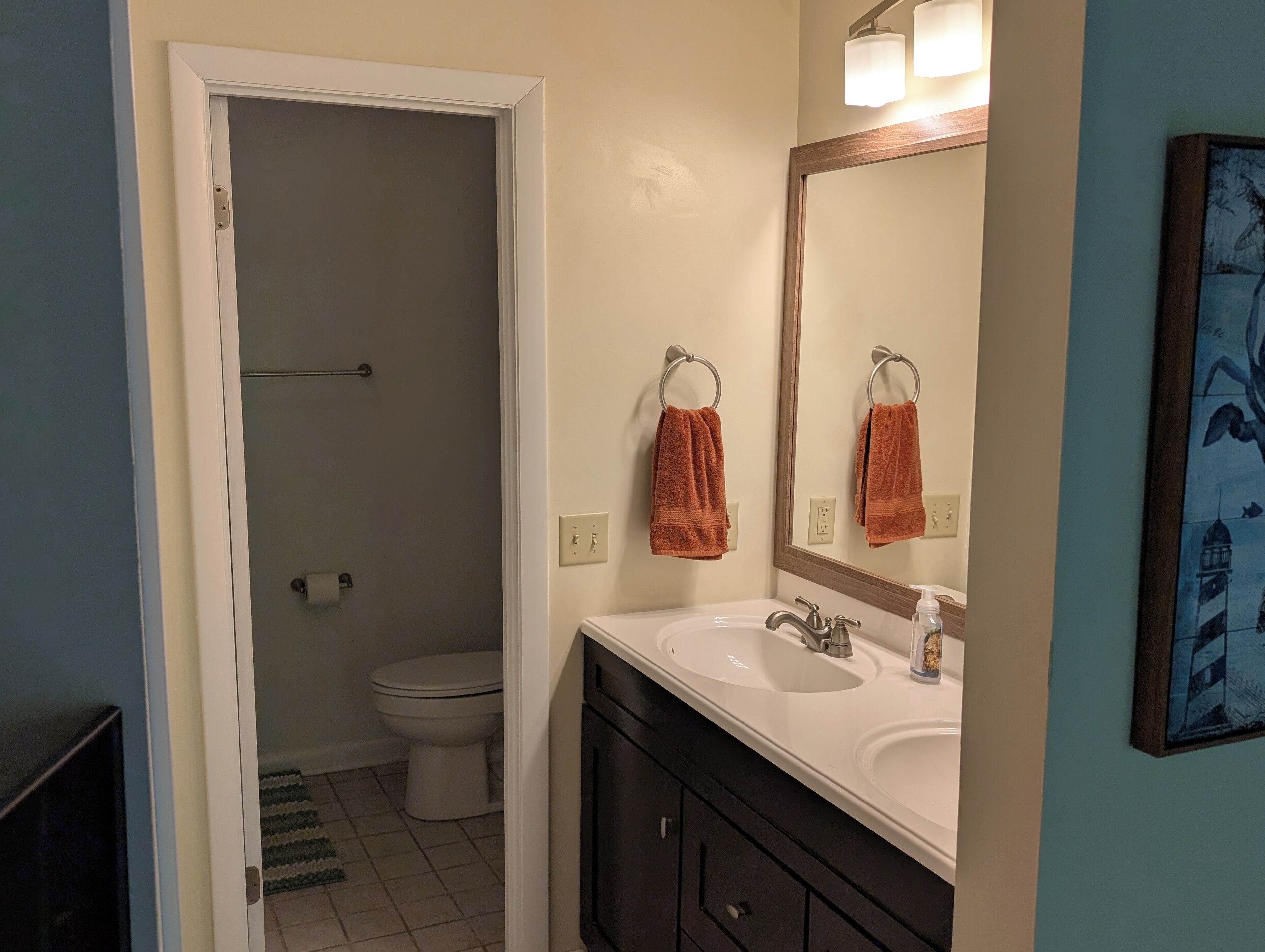 Ein Badezimmer mit Toilette, Waschbecken und Spiegel. Handtücher hängen an einem Handtuchhalter.
