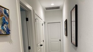 A hallway with white walls, carpeted floor, and doors leading to rooms. There are framed pictures on the walls. - Charming townhome.  3-bdrm, 2.5 bath with pool. 10 minutes to Kyle Field. (College Station)