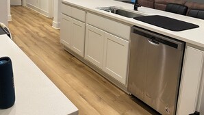 A modern kitchen with white cabinetry, a stainless steel dishwasher, and a black faucet. There is a wooden floor and a white countertop. - Charming townhome.  3-bdrm, 2.5 bath with pool. 10 minutes to Kyle Field. (College Station)