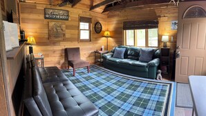 A cozy cabin interior with a leather sofa, a plaid rug, a wooden wall with a welcome sign, and a clock. - Charming cabin in delightful Duquette with AC near miles of ATV trails. (Kerrick)