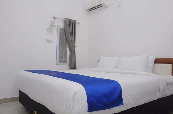 A neatly made bed with white and blue bedding, a grey curtain, and a wall-mounted air conditioner. - Desiring Homestay Banjarmasin (Banjarmasin)