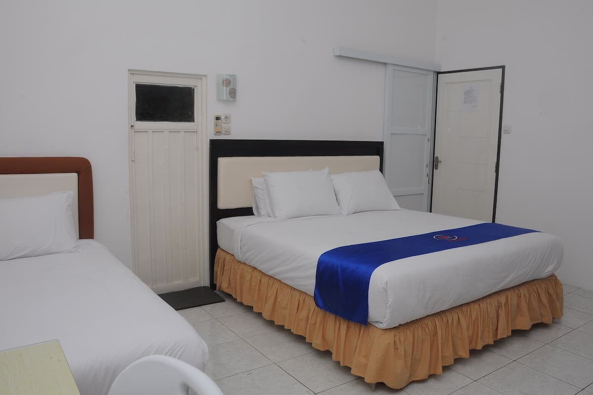 Hotelkamer met een enkel bed, nachtkastje, raam, deur en een airconditioning unit aan de muur.