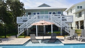 A swimming pool with a white deck, a covered seating area, and a staircase leading to a second level. - Book w/ Phone + Save 10%! Private Pool + Walk 2 Beach! (Gulf Shores)