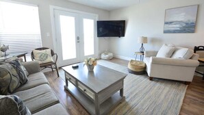 A living room with a sofa, a coffee table, a television, and a painting on the wall. - Book w/ Phone + Save 10%! Private Pool + Walk 2 Beach! (Gulf Shores)