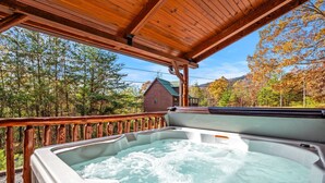 Een hottub onder een houten pergola met uitzicht op een huis en bomen.
