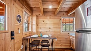Interieur van een houten hutje met een keukenhoek, een roestvrijstalen koelkast, houten wanden en een eettafel met stoelen.