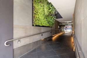 Stylish hallway with a handrail and vertical garden, leading to a glass door entrance.