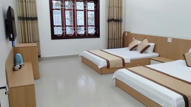 A hotel room with two single beds, a wooden nightstand, a television, and a window with decorative grills. - Anh Trang Hostel LS - by BAY LUXURY (Tam Thanh)