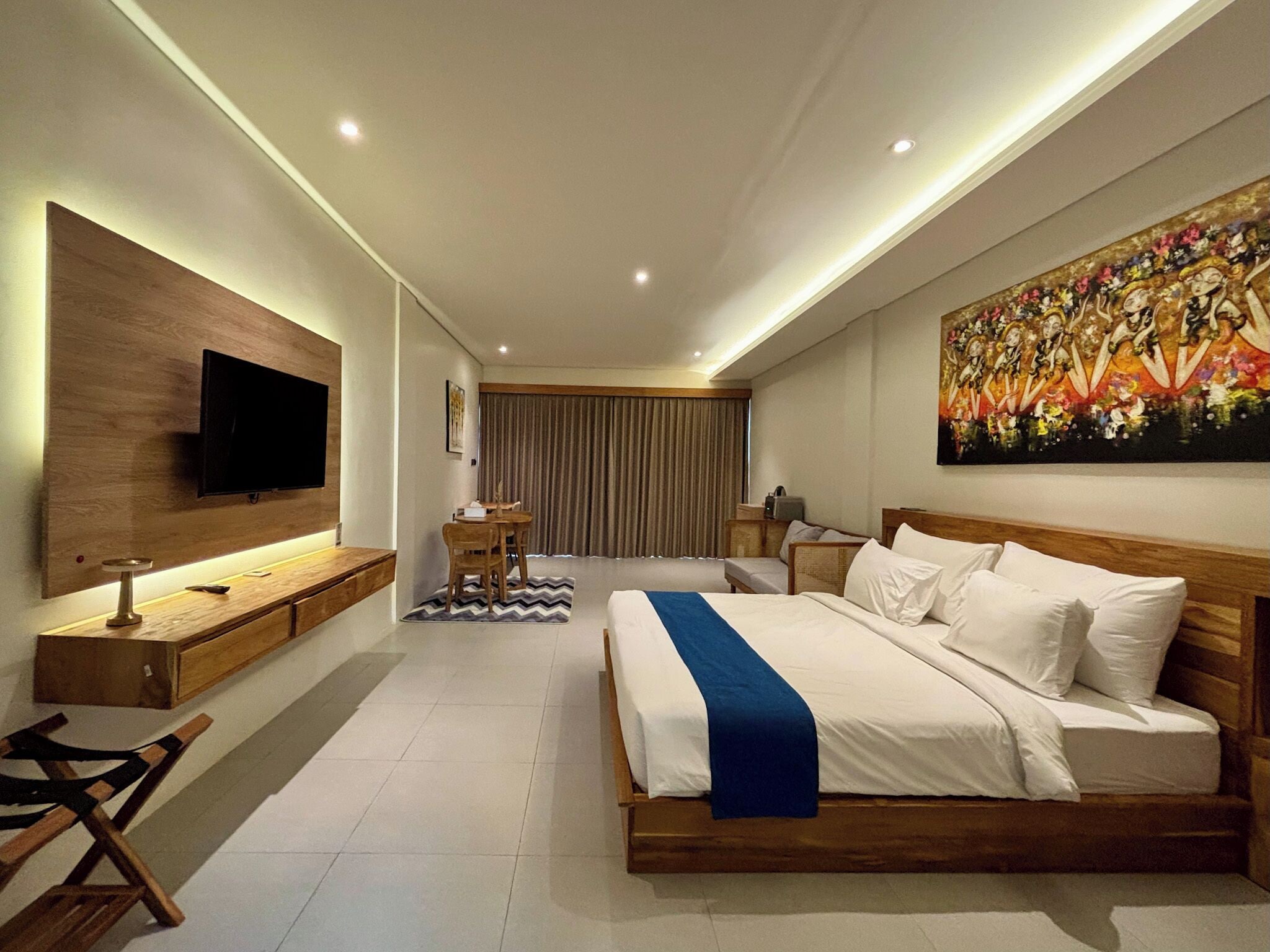 Una habitación de hotel moderna con una cama grande, un televisor de pantalla plana montado en la pared, un escritorio con una silla y un cuadro sobre la cama.