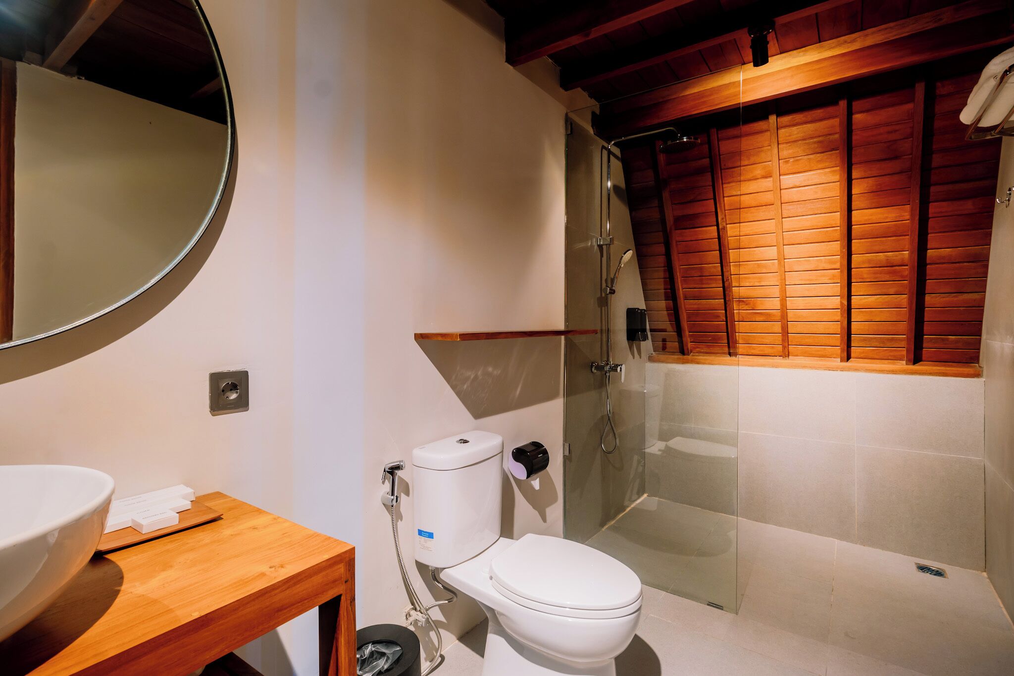 Ein modernes Badezimmer mit einem Holz-Waschtisch, einer weißen Toilette und einer Duschkabine aus Glas.