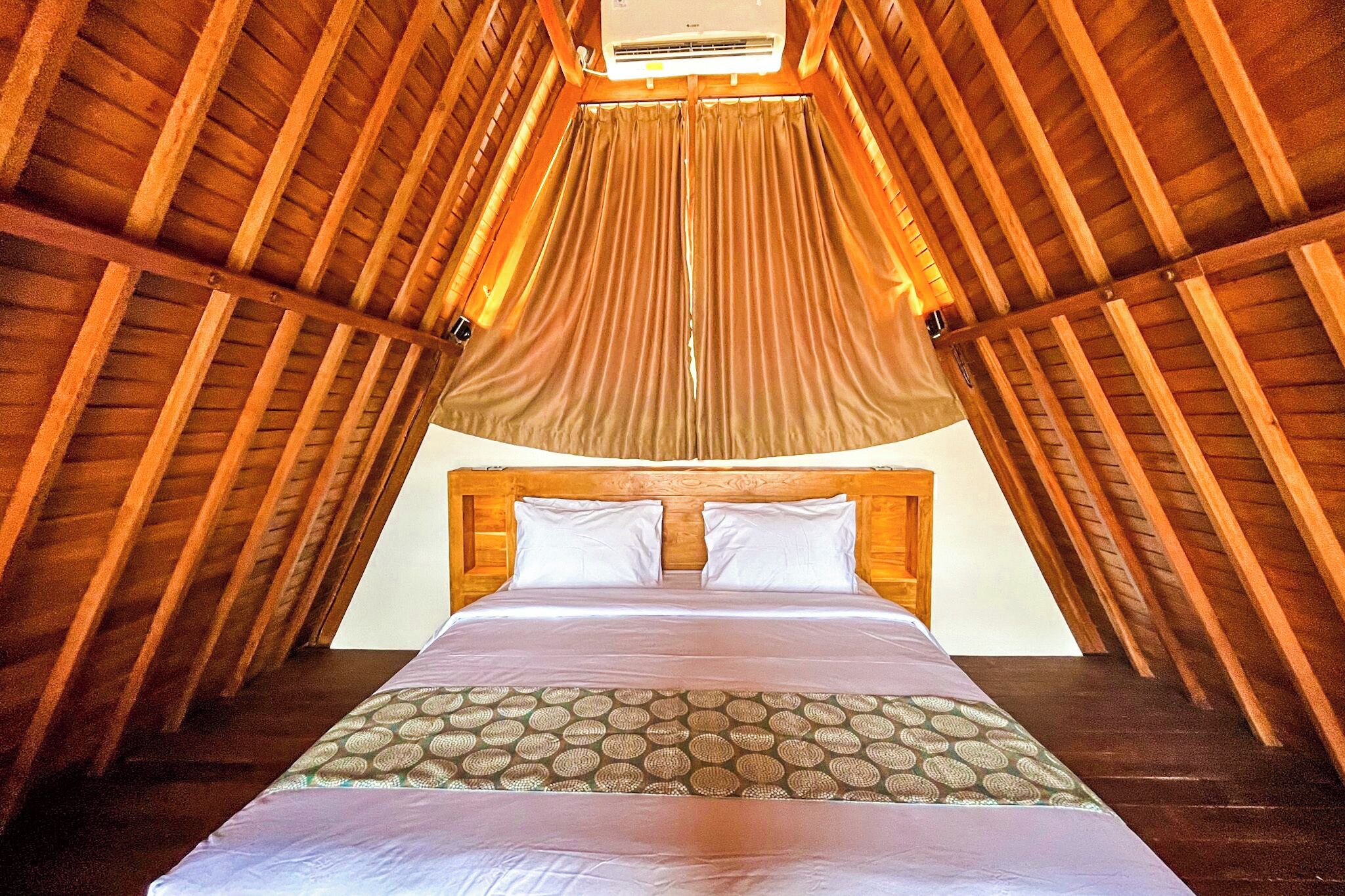A bedroom with a wooden ceiling, a bed with white bedding, and a patterned throw.