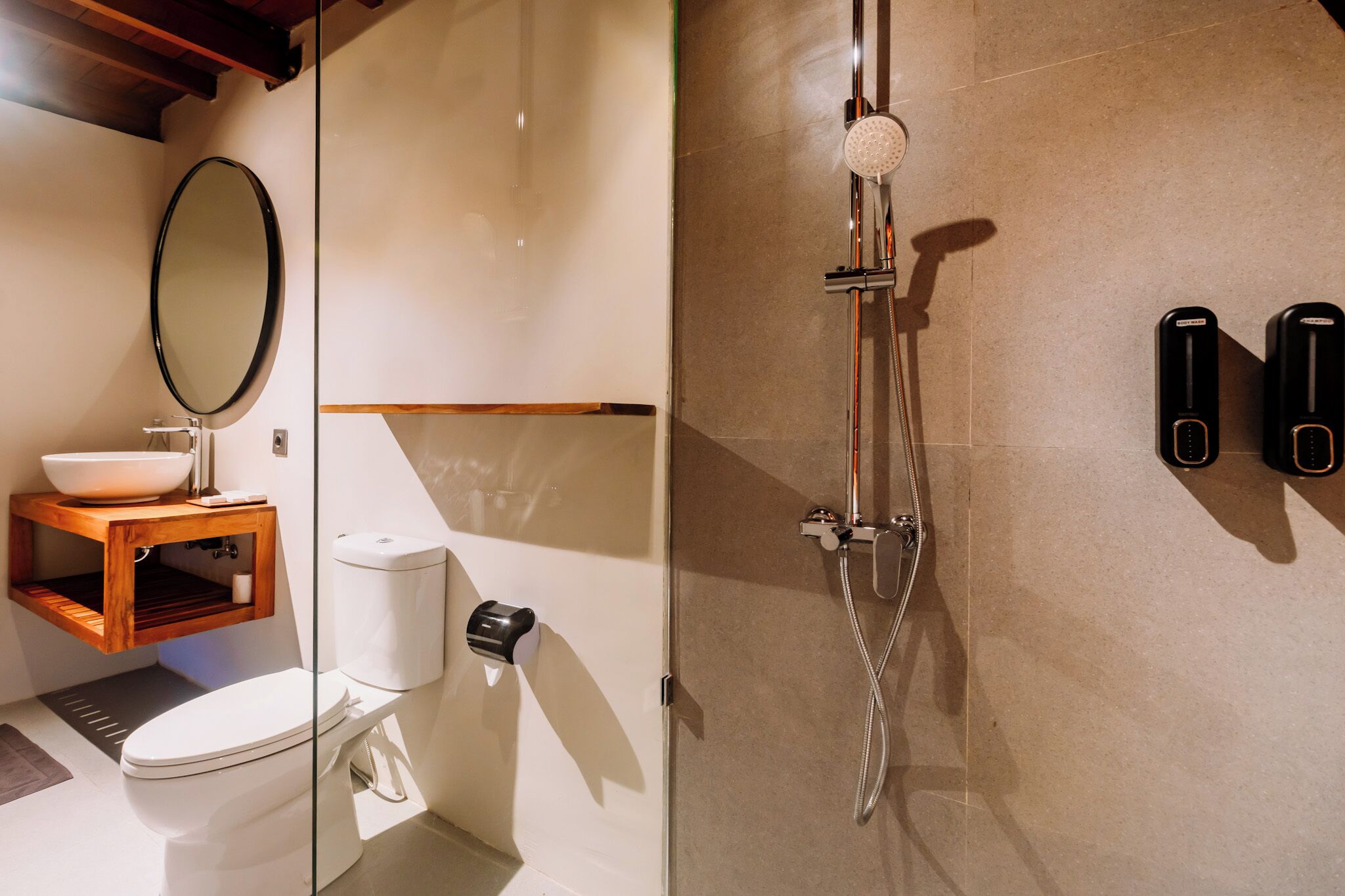Un baño moderno con cabina de ducha de vidrio, un mueble de tocador de madera y un inodoro blanco.