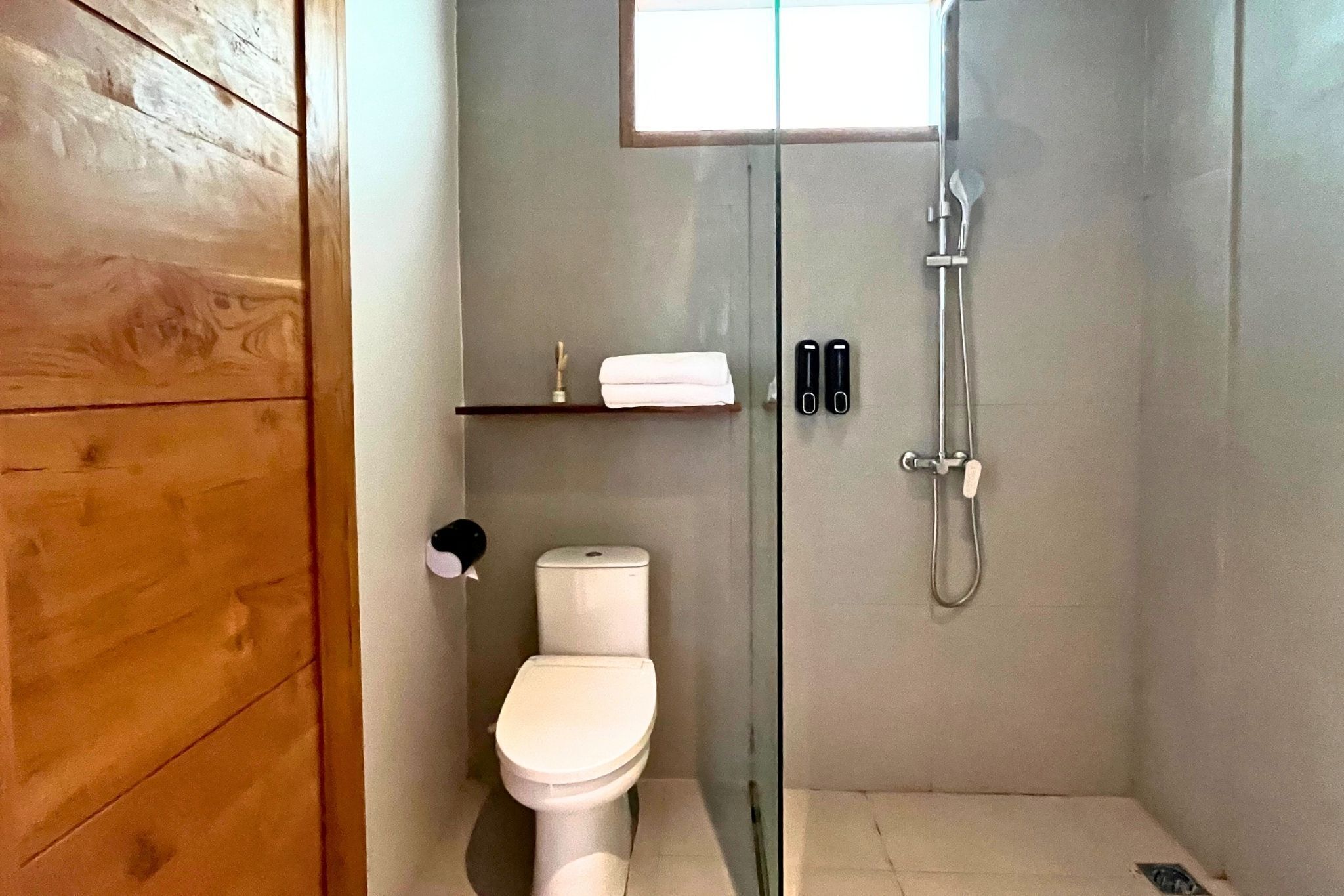 A small, modern bathroom with a toilet, a glass shower enclosure, and a wooden door.