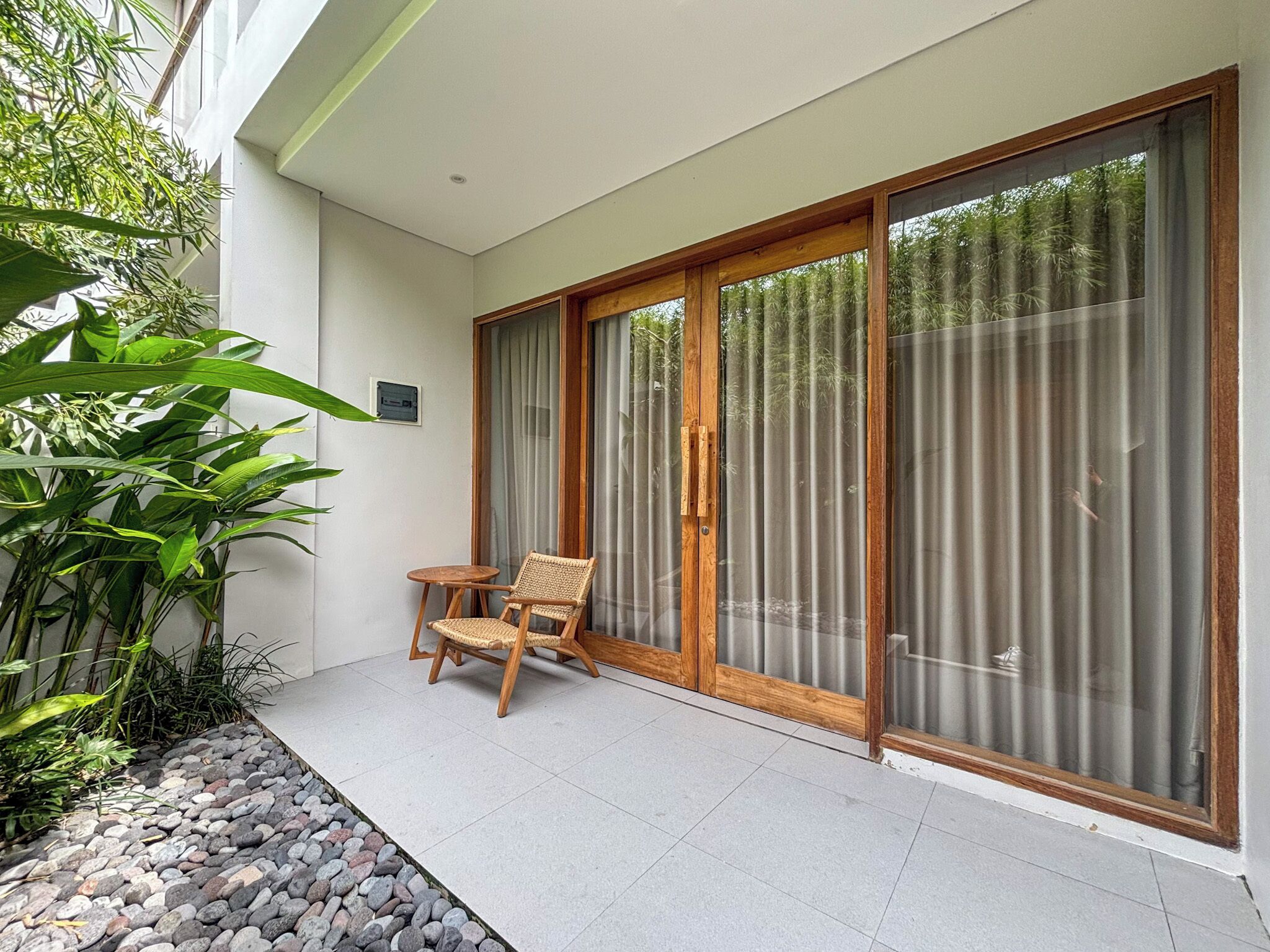 A balcony with a wooden chair, a small table, and a glass door with curtains.