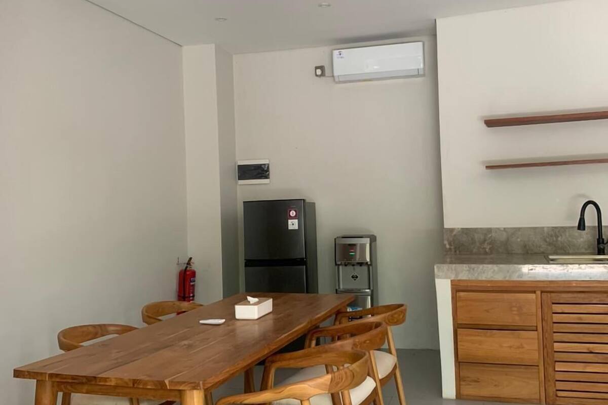 A dining area with a wooden table and chairs, a black refrigerator, a water dispenser, and a kitchen counter with a sink.