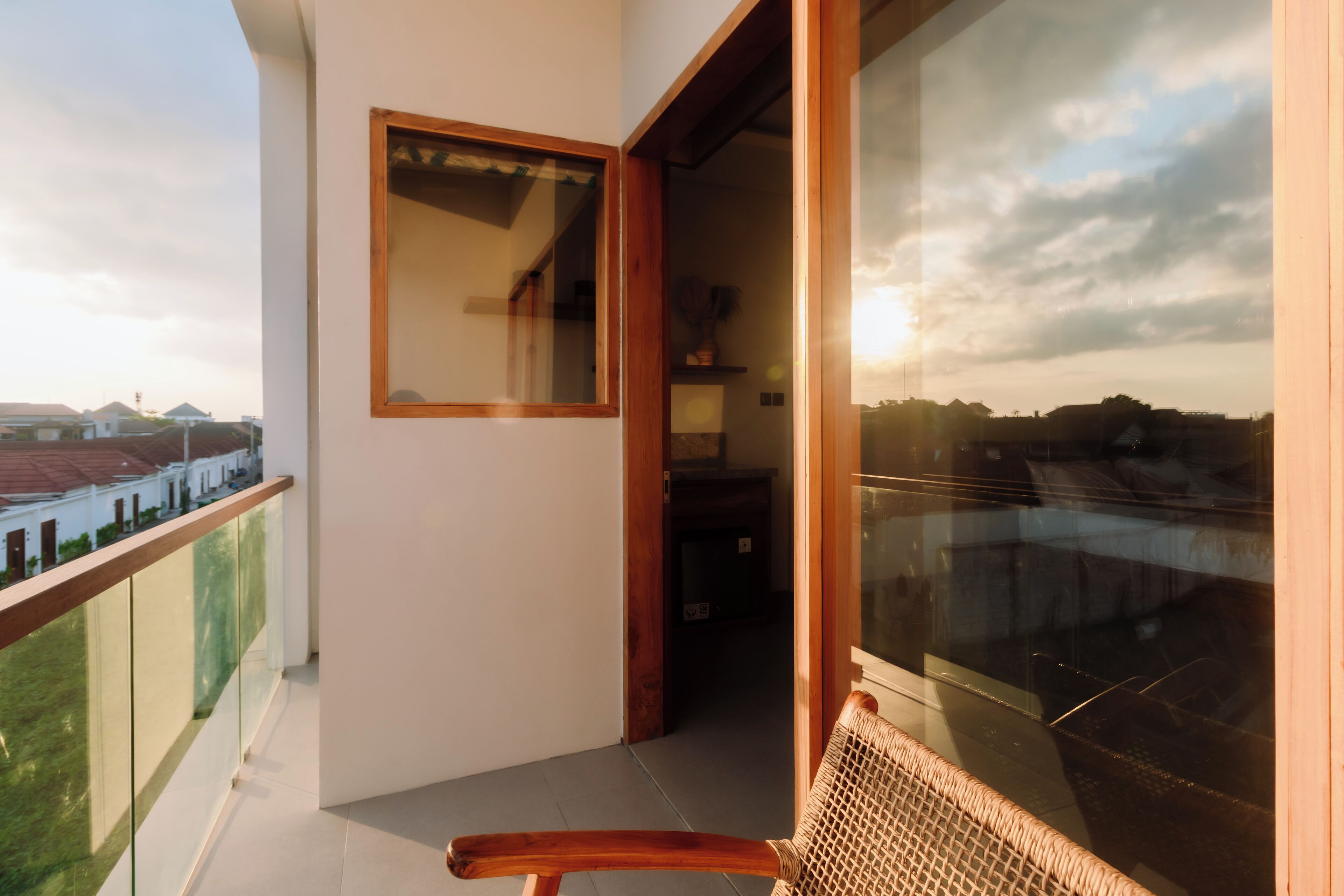 Een balkon met uitzicht op de stadsgezicht, een houten stoel en een glazen deur naar een binnenruimte.