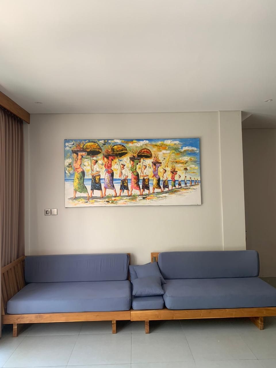 A room with a large painting of people on a beach, a wooden sofa, and a curtain.