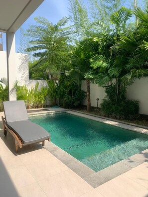 A pool with a lounge chair, surrounded by lush greenery and a white wall. - Campbar 4 (Munggu)