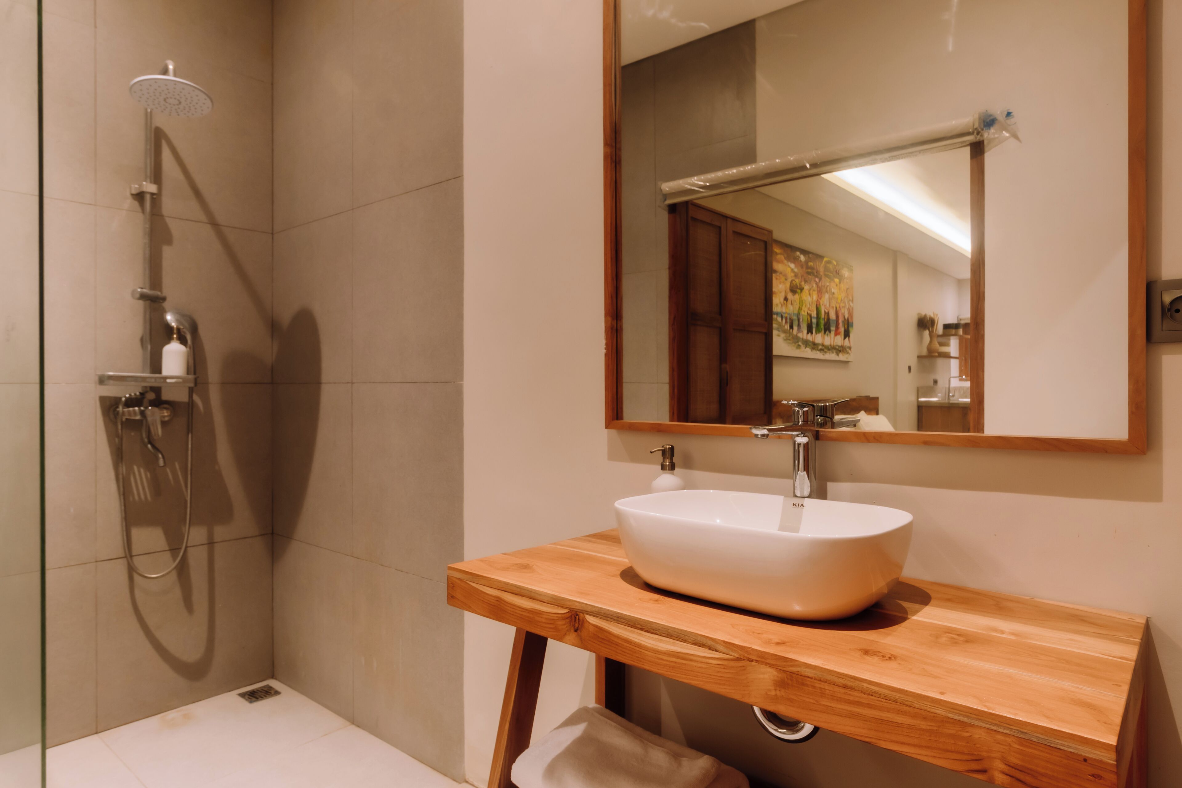 Un baño moderno con tocador de madera, un lavamanos blanco y una ducha con cabezal de ducha de mano.