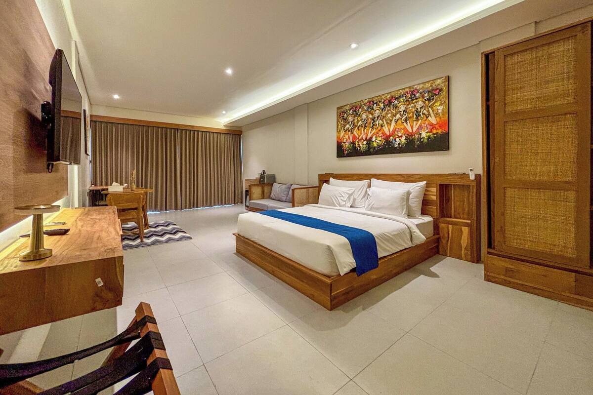 A modern hotel room with a large bed, a desk, a chair, a TV, and a painting on the wall.