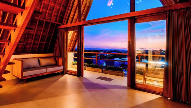 A spacious room with a large window offering a view of the cityscape, a wooden ceiling, and a built-in sofa. - Campbar 4 (Munggu)