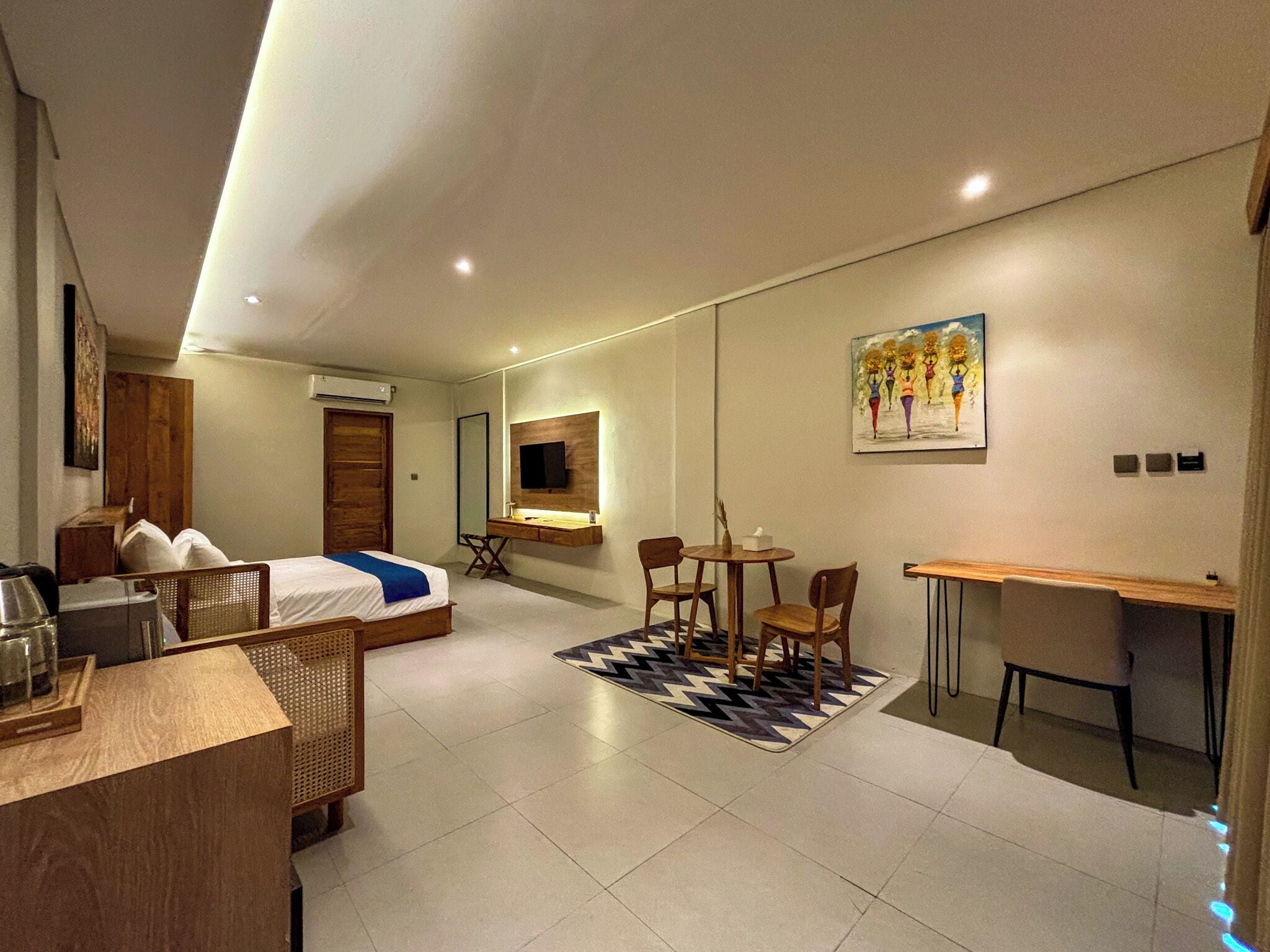 Ein modernes Hotelzimmer mit Bett, Schreibtisch, Stühlen, einem Spiegel und einem Bild an der Wand.