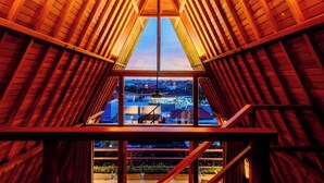A wooden interior with a central skylight and a view of a town below. - Campbar 4 (Munggu)